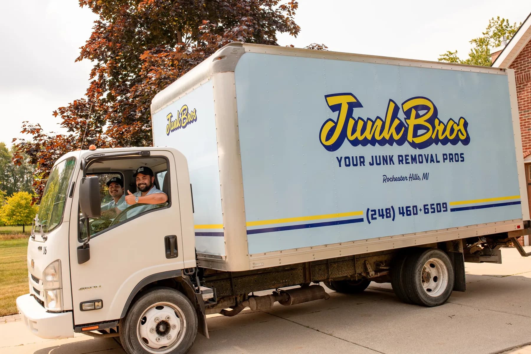 The wrapped Junk Bros box truck in a Rochester Hills driveway, Matt and Brad in the cab